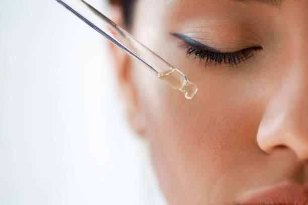 Close-up of a woman applying hyaluronic acid and vitamin C serum with a dropper to her face.